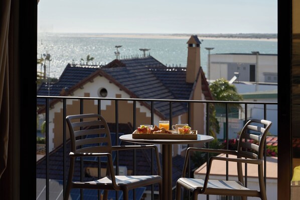 A balcony with a table and chairs, overlooking a coastal view with buildings and a beach. - Macià Doñana (Sanlucar de Barrameda)