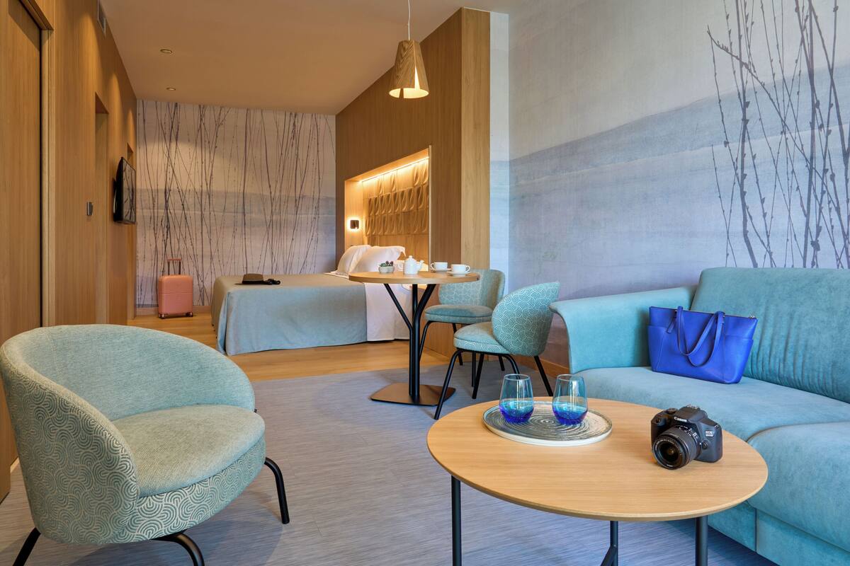 Una habitación de hotel moderna con sofá, sillón y una mesa con cámara y vasos.