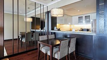 A modern dining area with a dark wooden table and chairs, a glass partition, and a kitchen with stainless steel appliances.