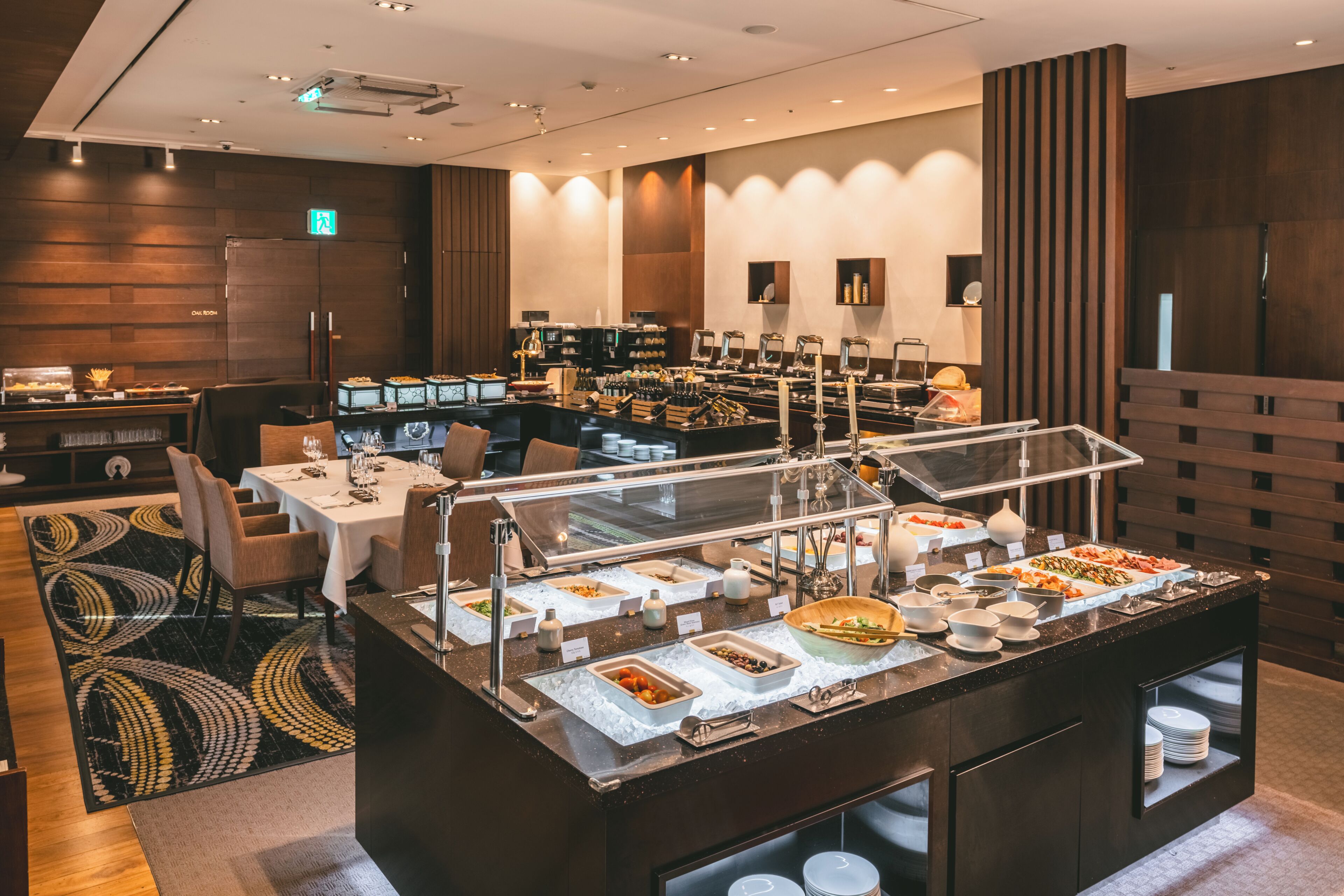 A buffet area with various food stations, a seating area with tables and chairs, and a refrigerator in the background.