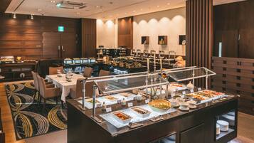 A buffet area with various food stations, a seating area with tables and chairs, and a refrigerator in the background.