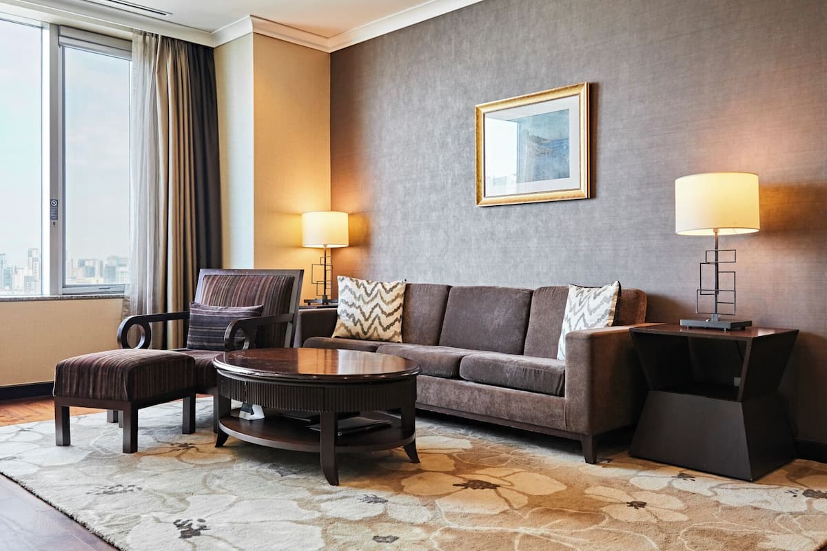 A modern hotel room with a sofa, armchair, coffee table, and two lamps.