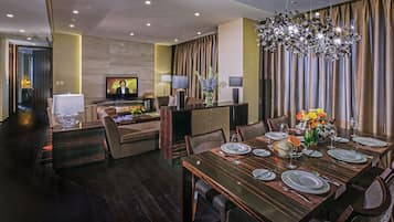 A modern dining area with a wooden table set for six, a television in the background, and a decorative chandelier.
