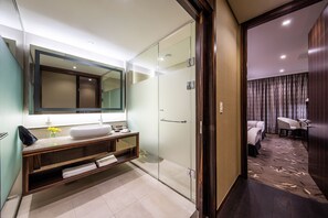 Un baño moderno con cabina de ducha de vidrio, un espejo grande y un tocador con lavamanos y perchero para toallas.