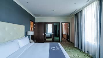 A hotel room with a bed, a nightstand, a lamp, a door leading to another room, and a view of a hallway.