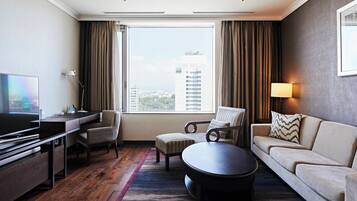 A hotel room with a large window, a flat-screen TV, a desk, a sofa, and a coffee table.