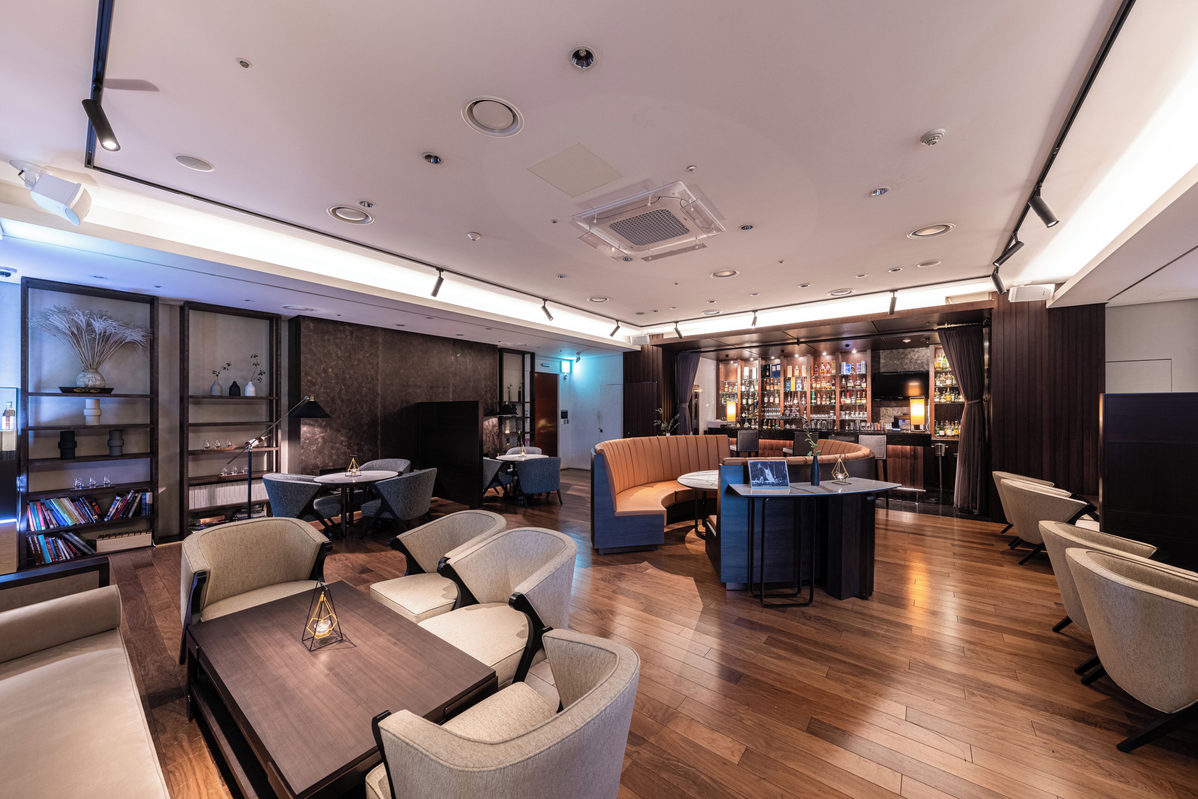 Un moderno vestíbulo de hotel con una zona de bar, espacios de descanso y una estantería.