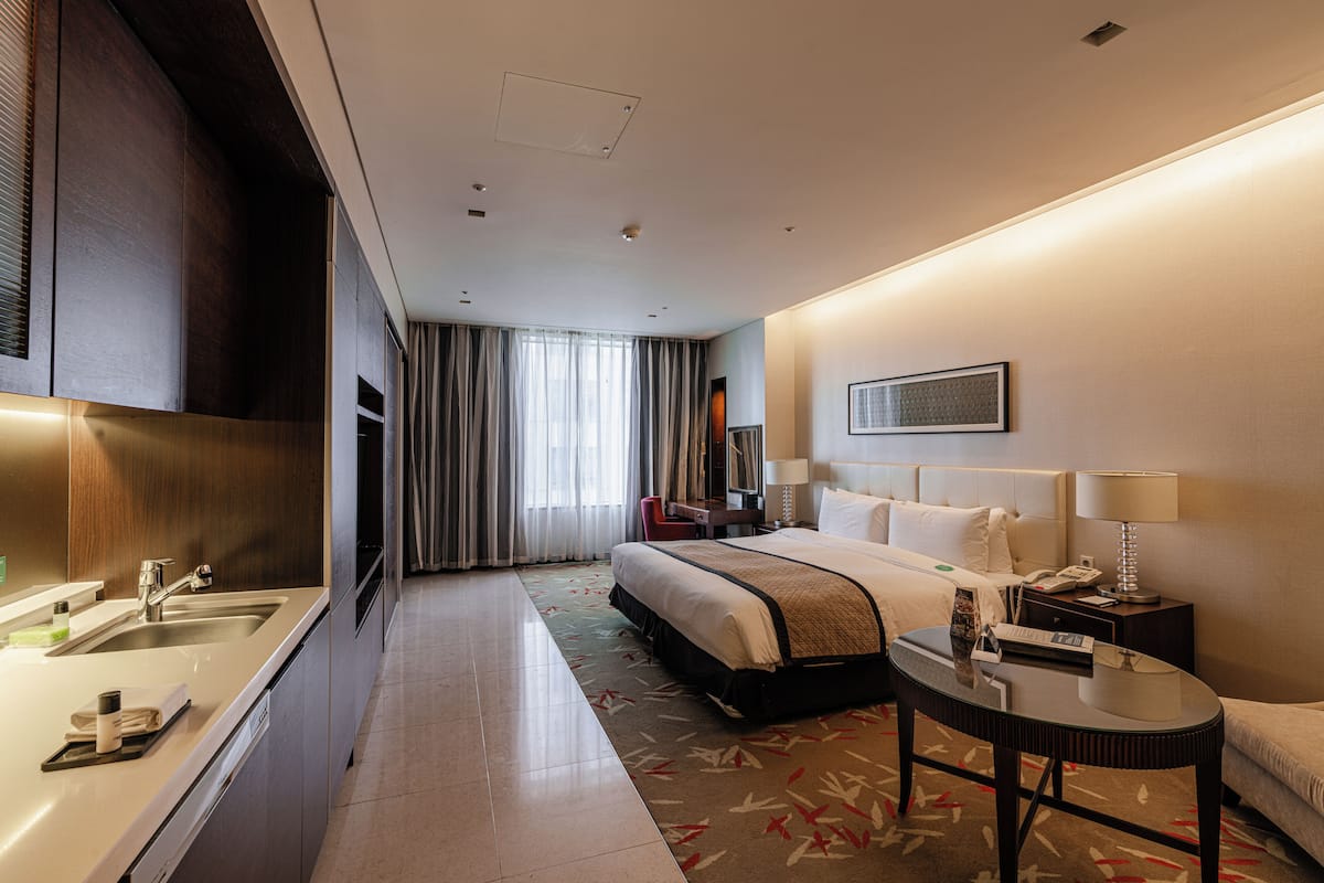 A hotel room with a bed, bedside table, lamp, and a view of the cityscape through the window.