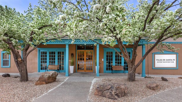 A building with turquoise doors and windows, a sign reading "Villas de Santa Fe Hilton Vacation Club", and a paved entrance area with large rocks and trees. - Hilton Vacation Club Villas de Santa Fe (Santa Fe)