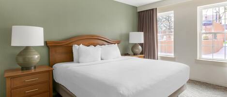 A hotel room with a large bed, two bedside tables with lamps, a ceiling fan, and a view of the outside.