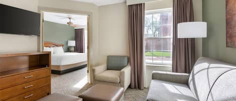 Una habitación de hotel con cama, sofá, sillón, escritorio y televisor.