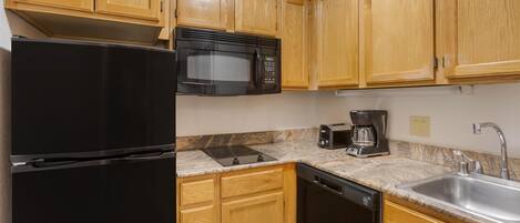Una cocina con armarios de madera, un refrigerador negro, microondas, cafetera y lavavajillas.