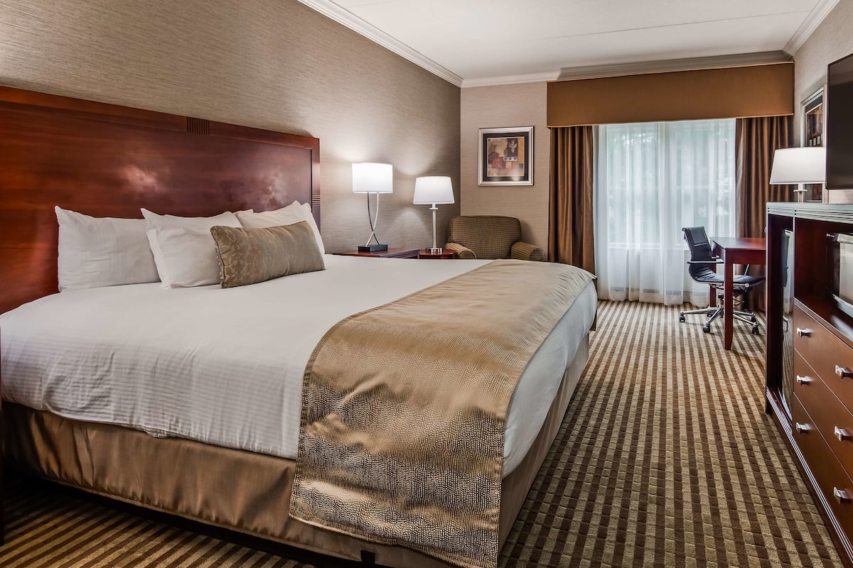 A hotel room with a large bed, two bedside lamps, a desk with a chair, a television, and a minibar.