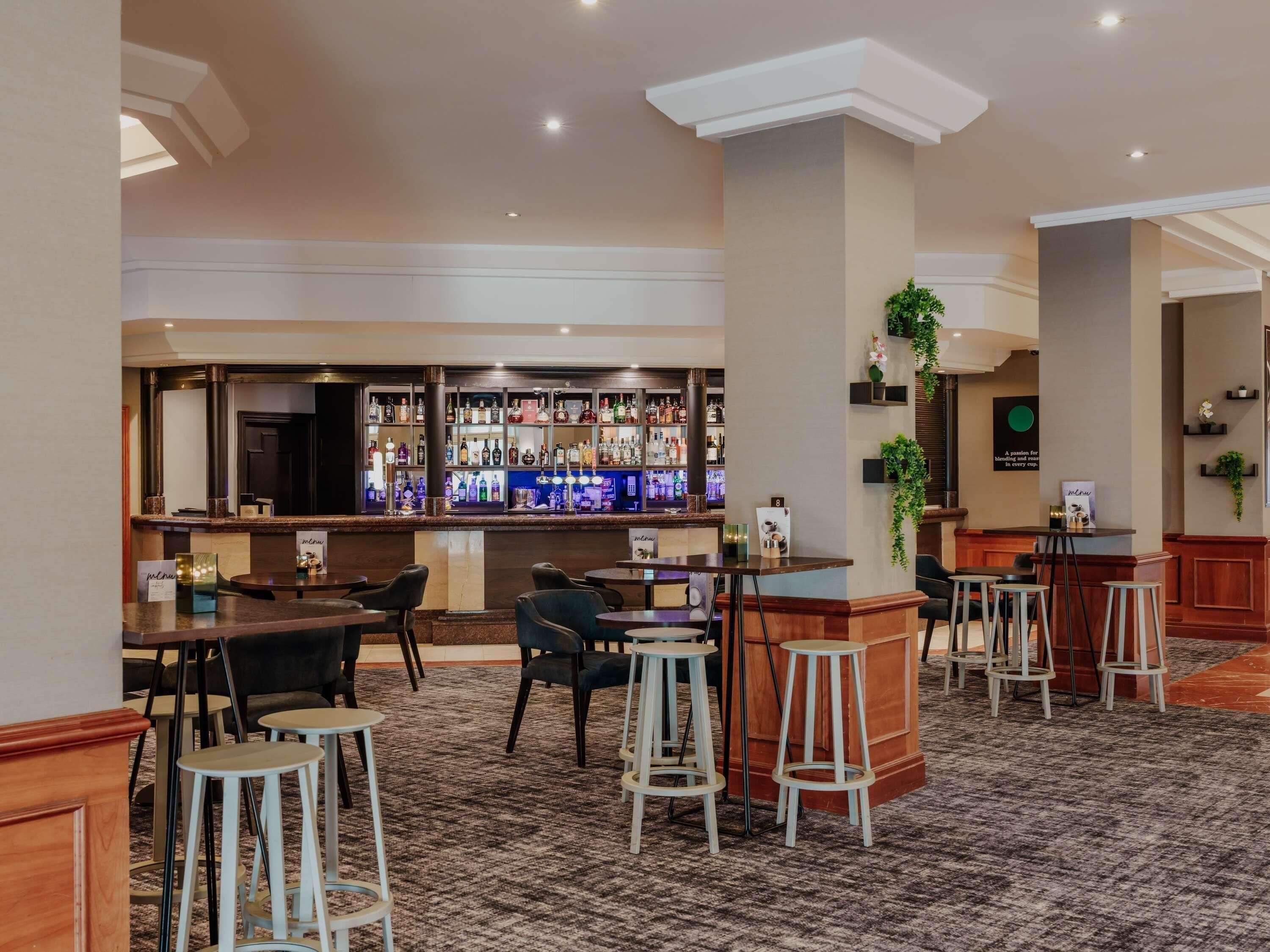 A bar area with multiple stools and tables, a bar counter with various bottles, and a carpeted floor.