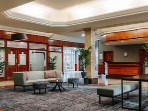 A lobby with a sofa, chairs, a coffee table, a reception desk, and potted plants. - Mercure Daventry Court Hotel (Daventry)