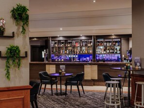 A bar area with multiple shelves of liquor bottles, a menu sign, and several seating options including chairs and stools. - Mercure Daventry Court Hotel (Daventry)