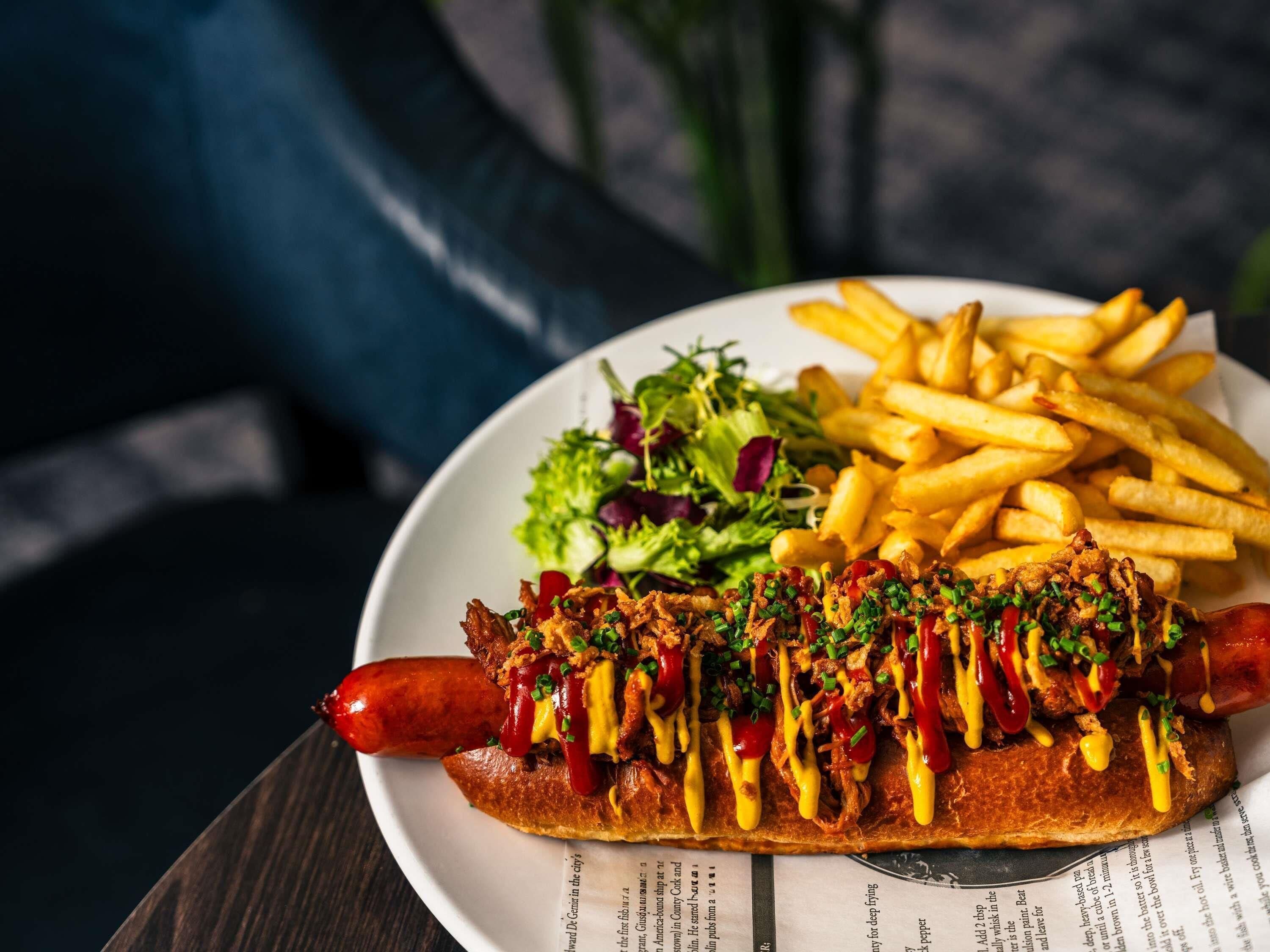 Un hot dog con ingredientes y papas fritas en un plato.