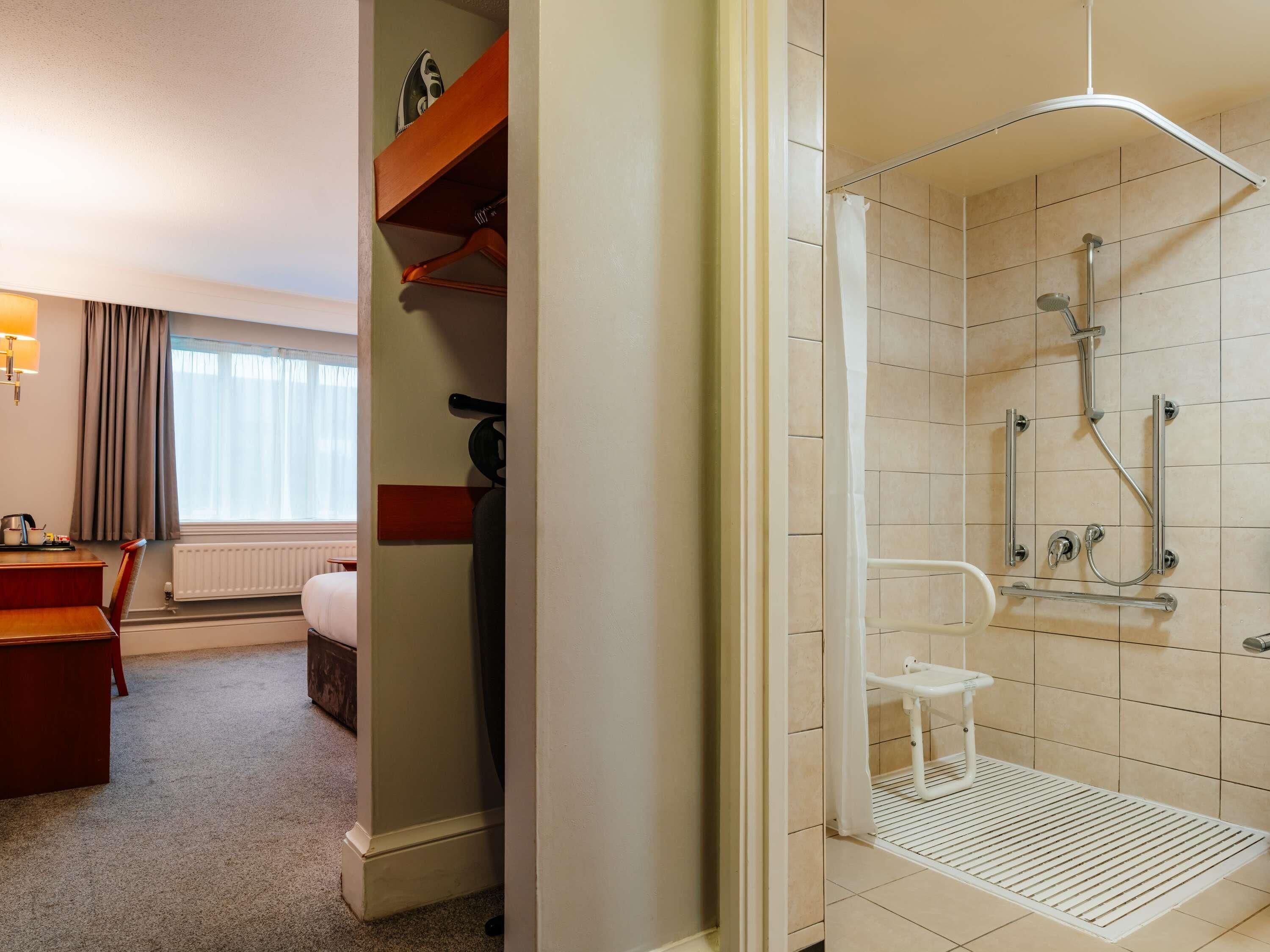 A hotel room with a shower, a bed, a desk, and a chair.
