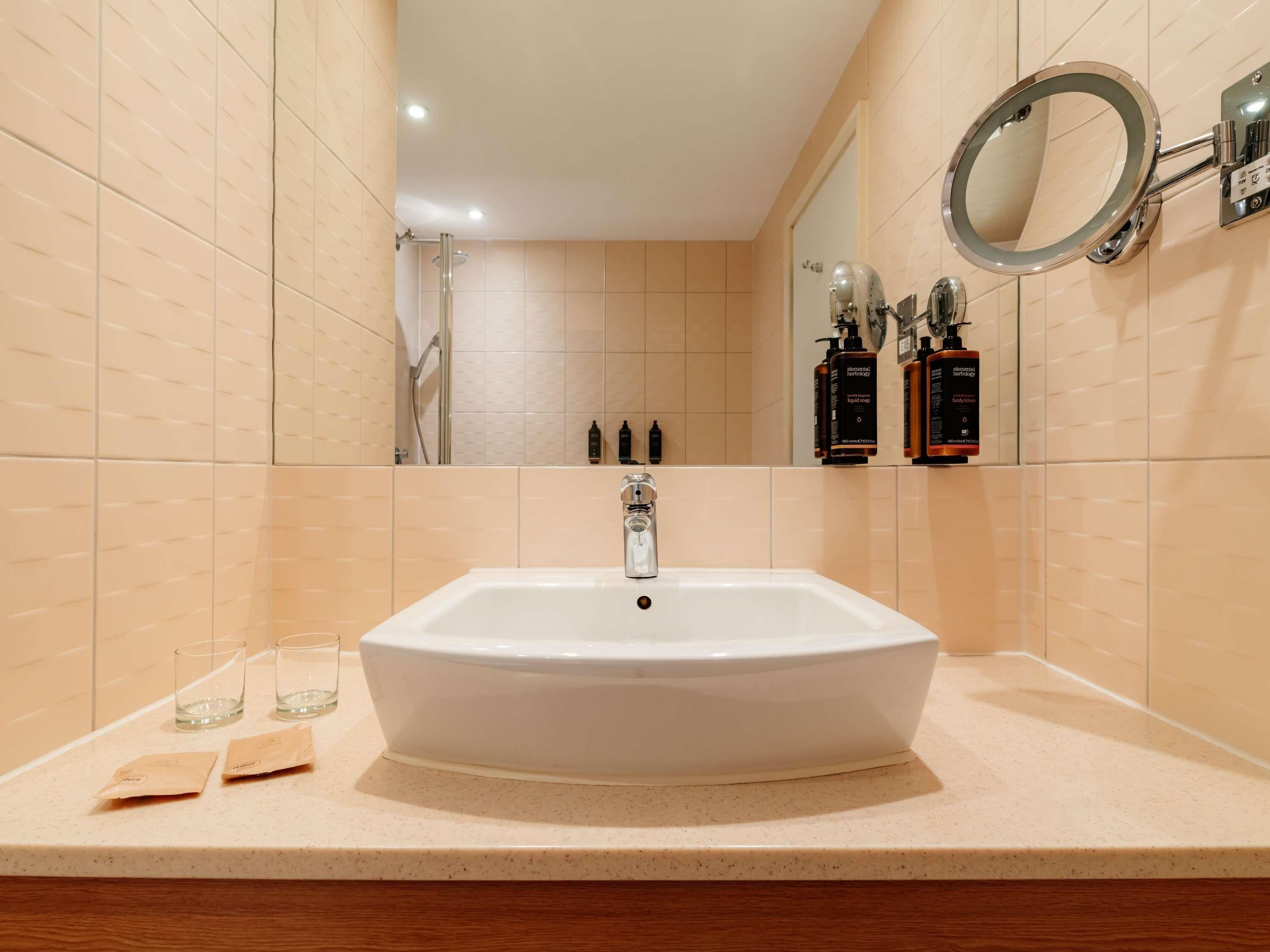 Un baño con un lavamanos grande de color blanco, un espejo y artículos de aseo en la pared.