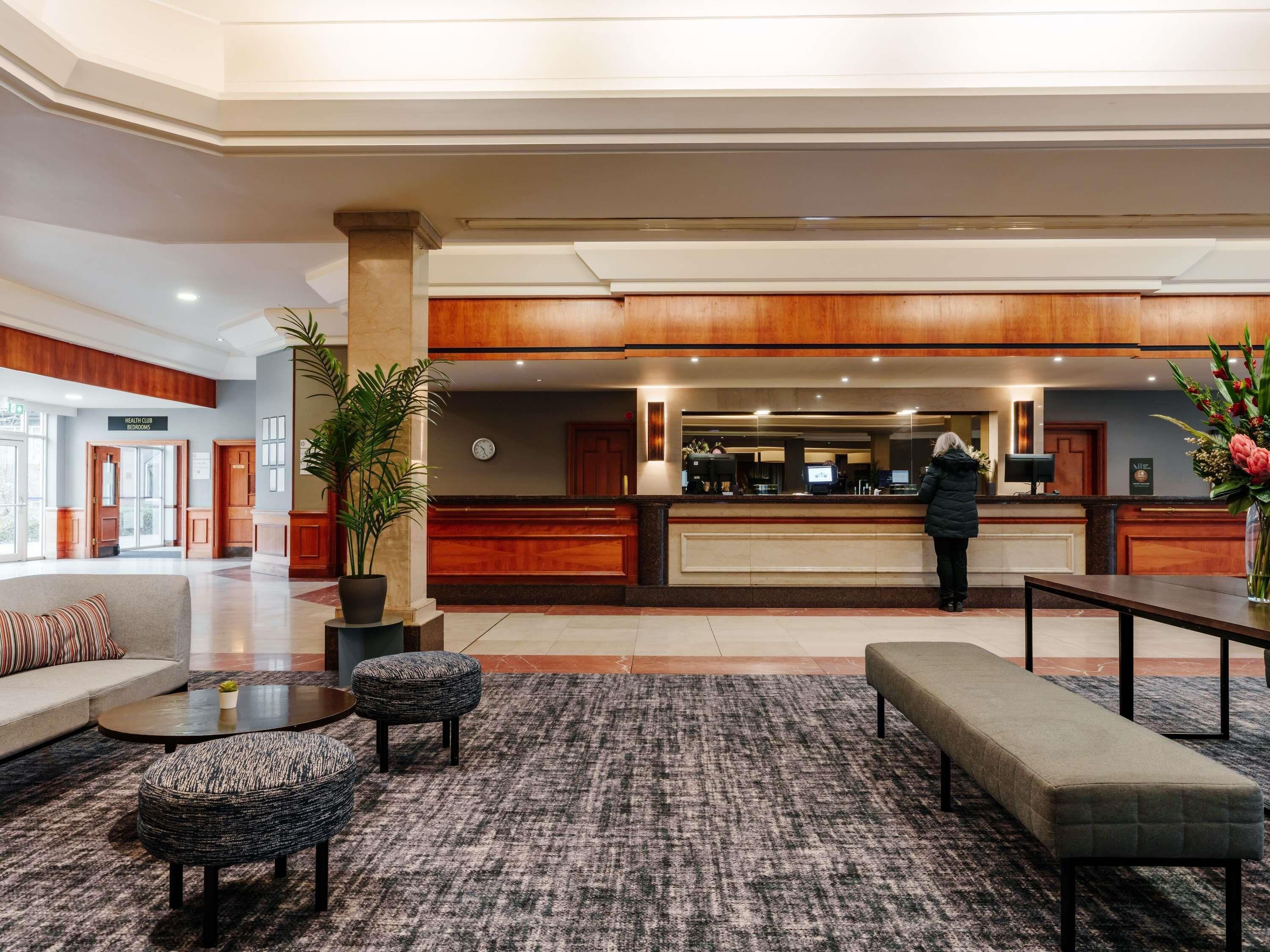 A hotel lobby with a reception desk, a sofa, a coffee table, and a bench.