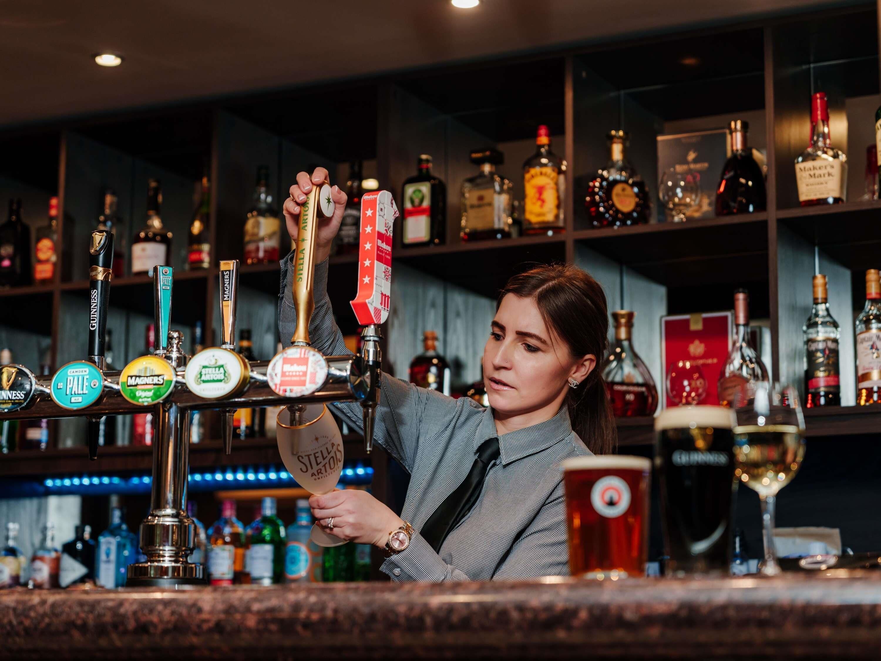 A bartender pouring beer from a tap with various brands visible.