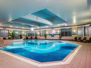 Piscina interna com chão de azulejos, relógio na parede e espreguiçadeiras à beira da piscina.