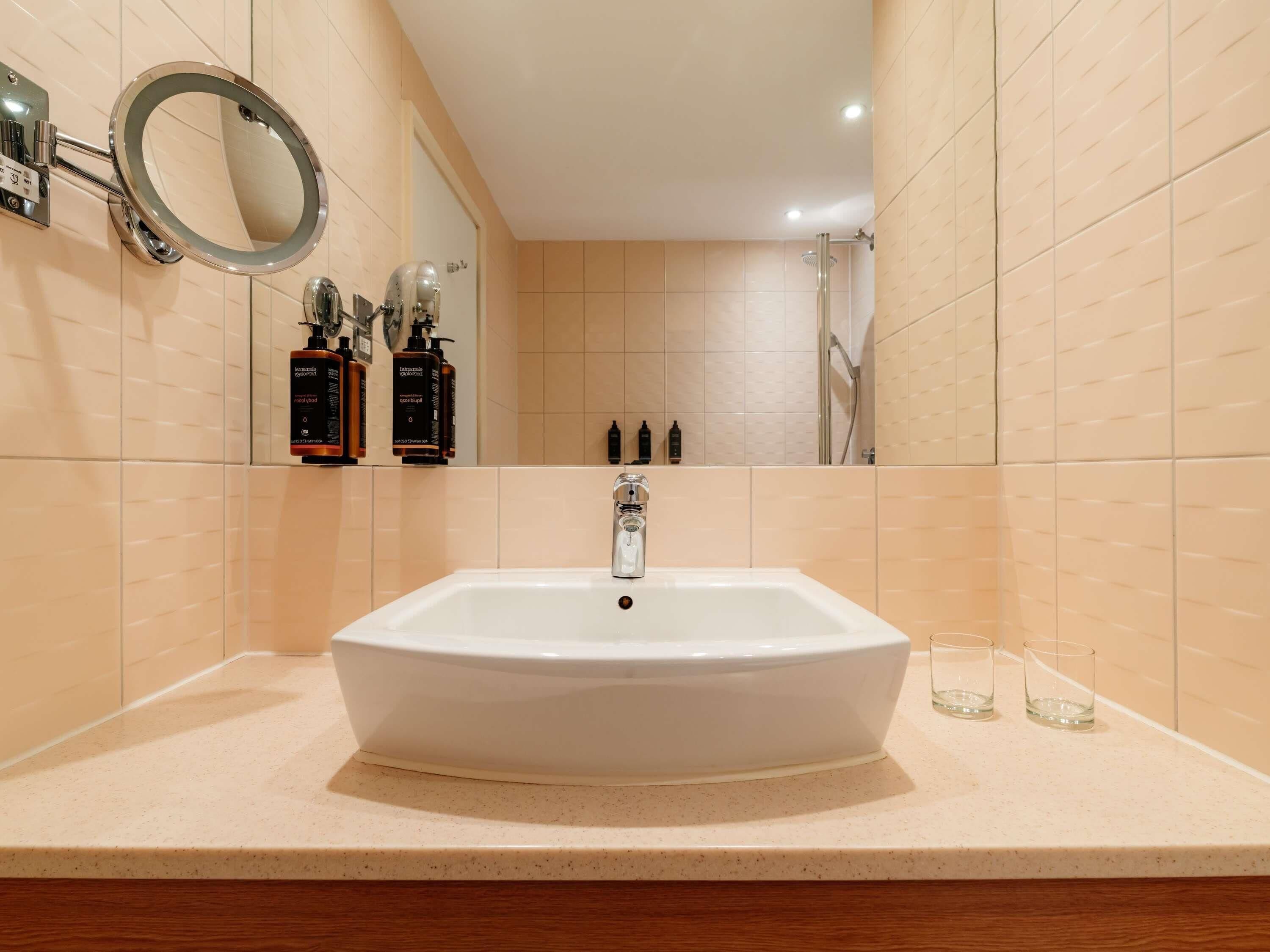 A bathroom with a white sink, a round mirror, and a shower.