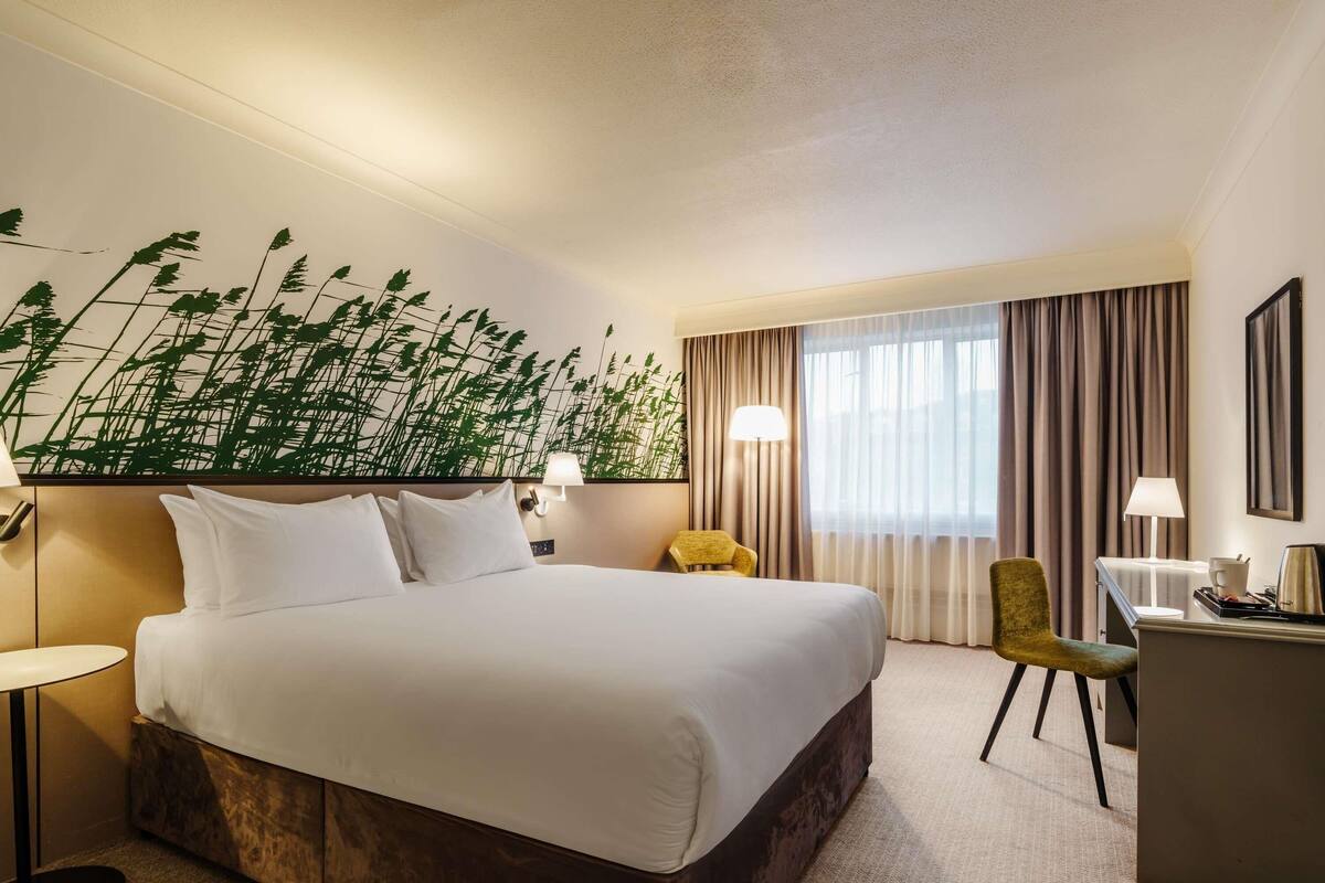 Una habitación de hotel con una cama grande, un escritorio con lámpara, una silla y una lámpara de pared.