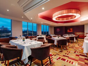 A restaurant with tables set for dining, large windows, and a view of the outside.