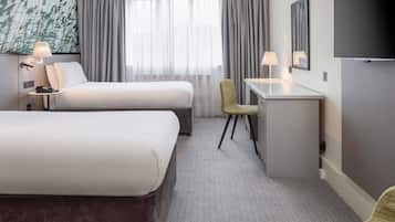 A hotel room with two beds, a desk, a chair, a TV, and a window with curtains.