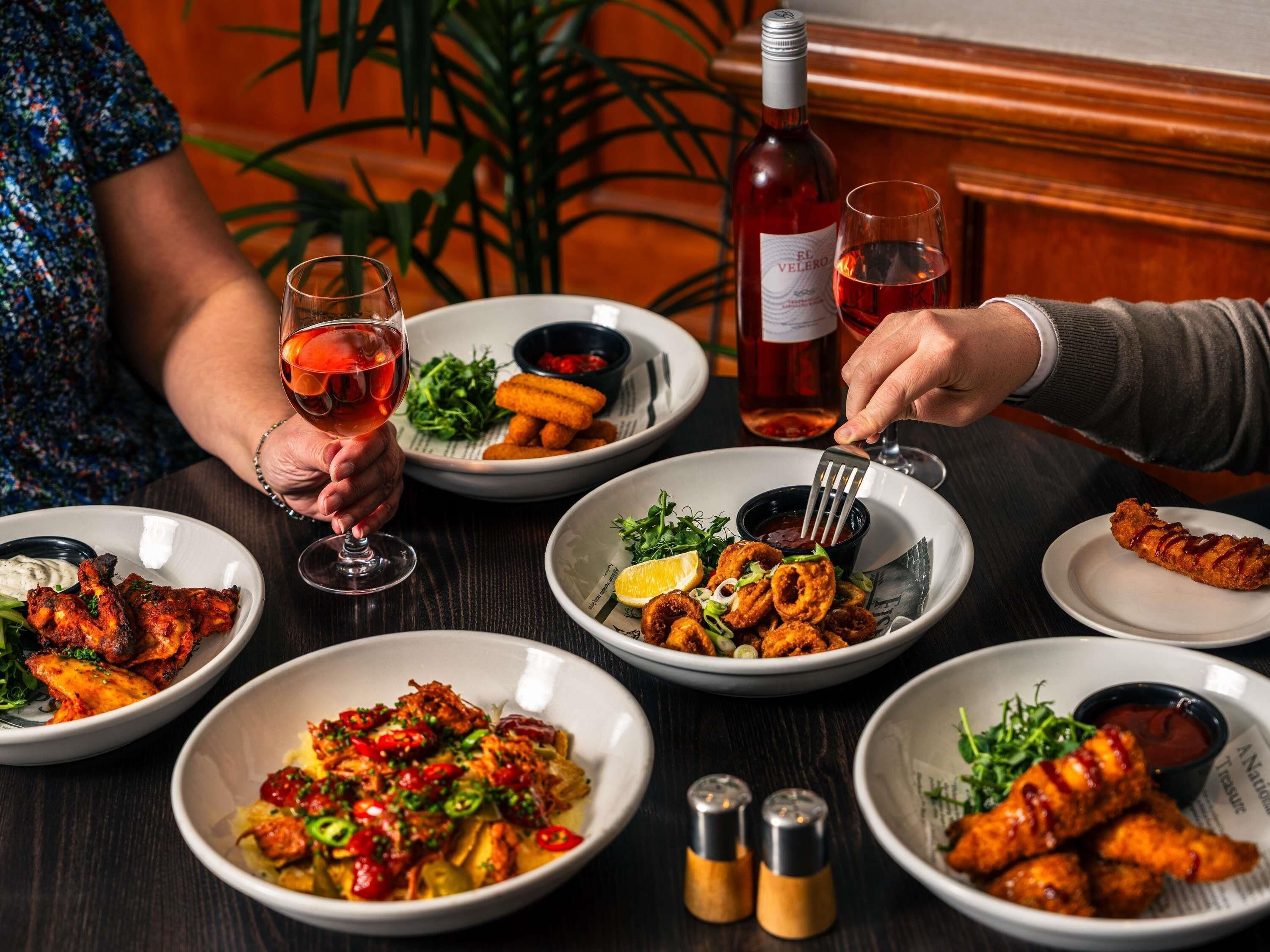 A dining table with various dishes, a bottle of wine, and two people dining.