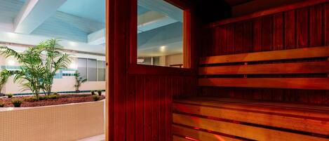 Una escalera de madera que sube a un nivel superior, suelo de baldosas y vista de un edificio con ventanas y plantas.