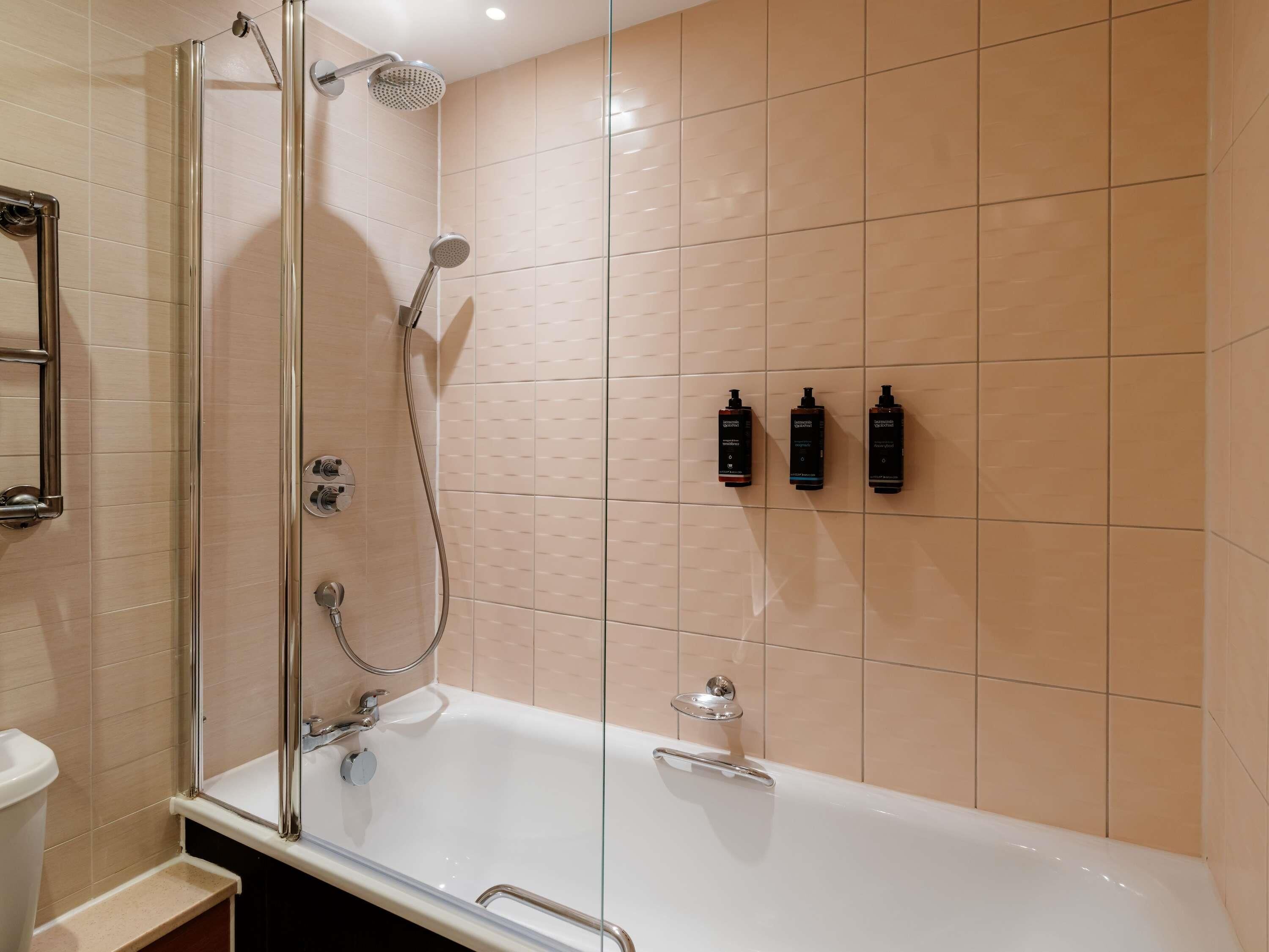A modern bathroom with a glass-enclosed shower, a white bathtub, and three toiletry bottles on the wall.
