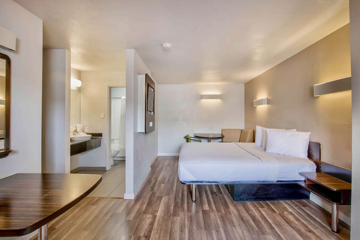 Una habitación de hotel moderna con cama, mesita de noche y un pequeño escritorio con silla.