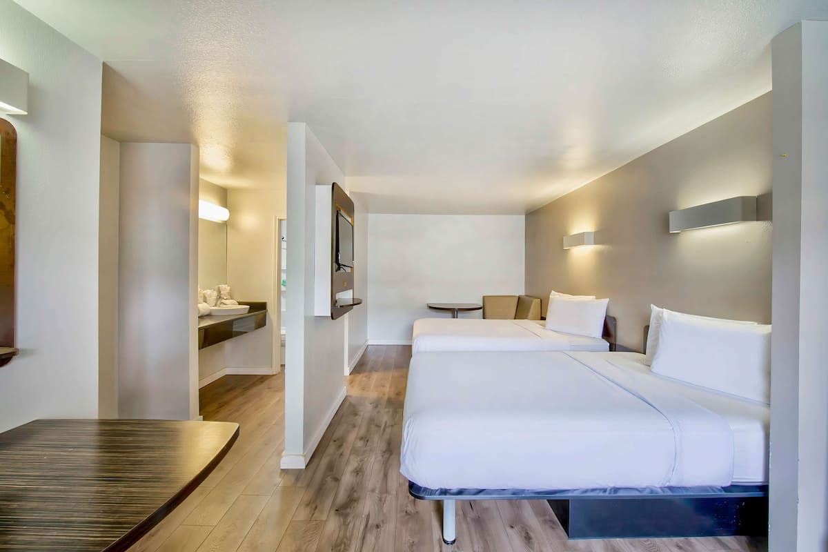 Habitación de hotel con cama, una mesita, una silla, escritorio, espejo y televisor montado en la pared.