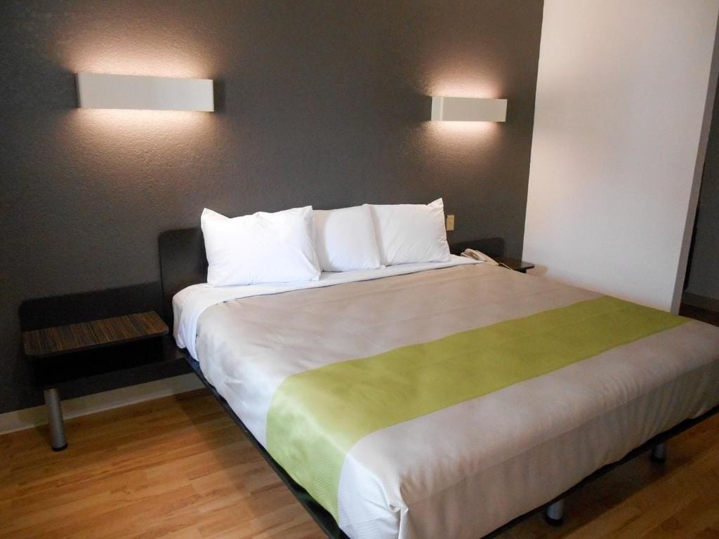 Hotellihuone, jossa on sänky, yöpöydät ja seinään kiinnitetyt valaisimet.