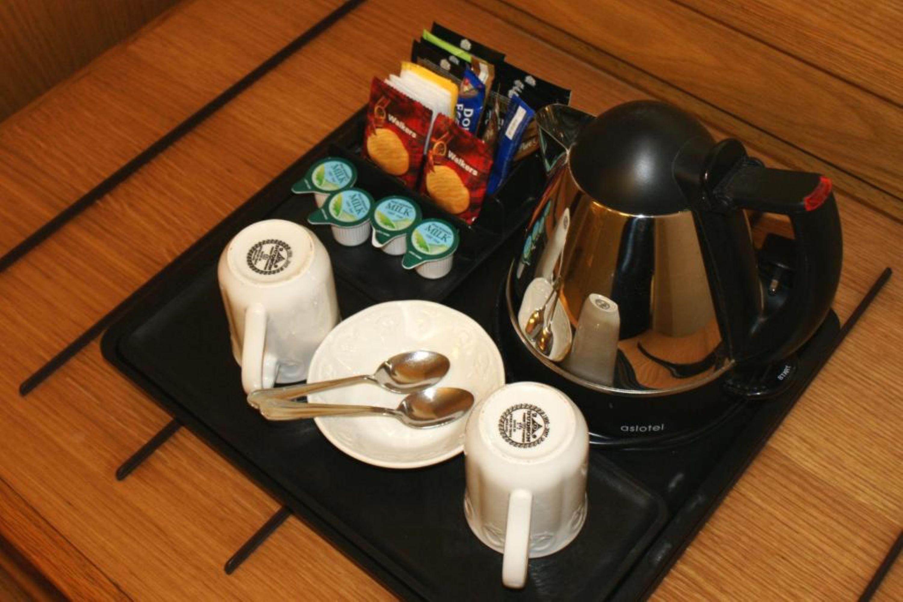 A tray with a coffee maker, two mugs, a plate with a spoon, and several food packets.