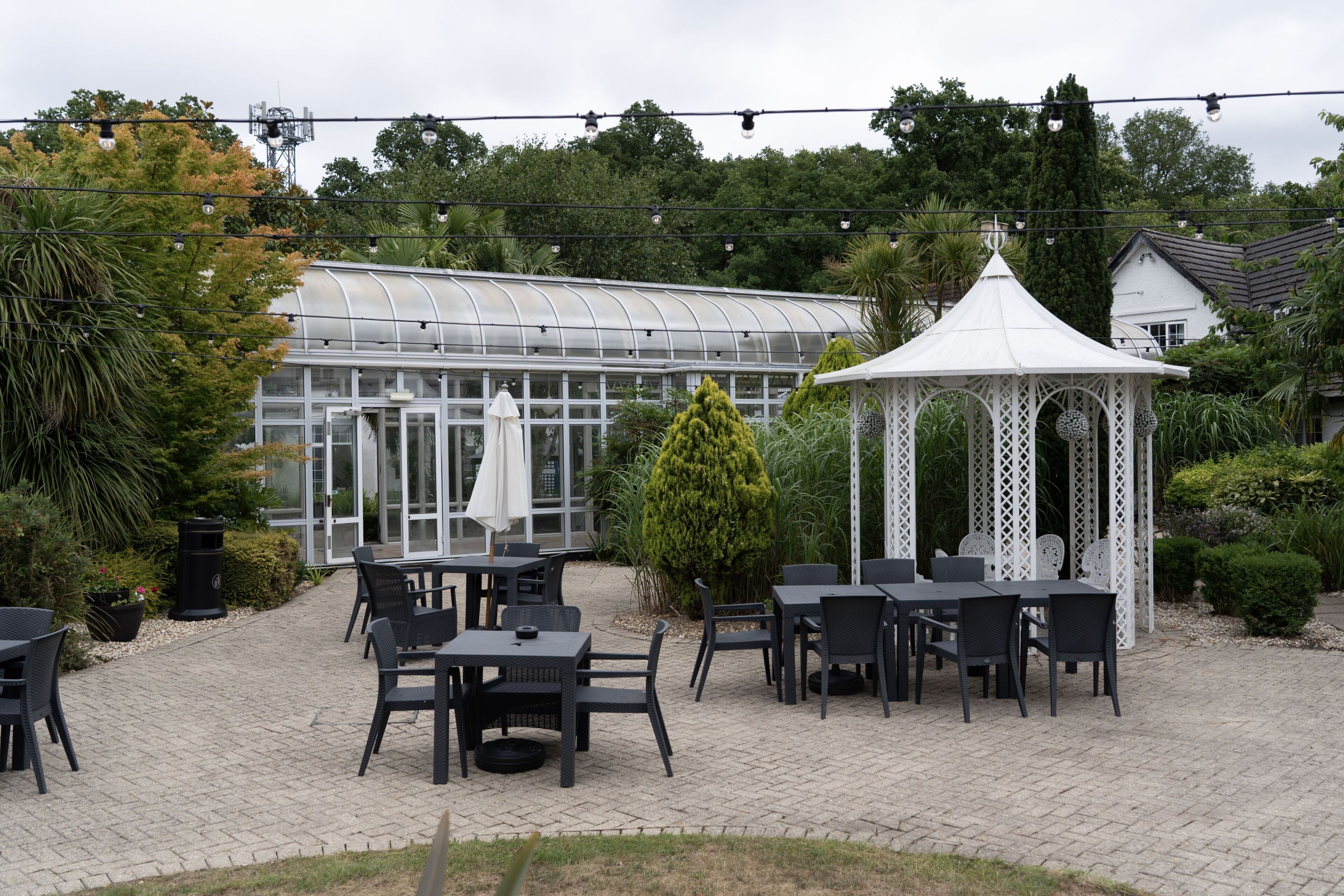 A greenhouse, outdoor seating area, and a white gazebo in a garden setting.