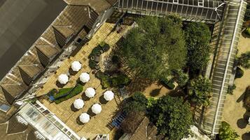 An aerial view of a rooftop garden with multiple white umbrellas, a greenhouse structure, and surrounding greenery.