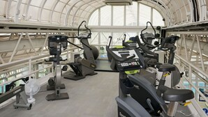 A gym with exercise equipment, a fan, and a large arched window. - Basingstoke Hotel (Hook)