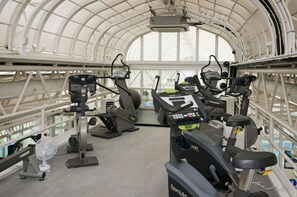 Un gimnasio con equipo de ejercicio, un ventilador y un amplio ventanal de arco.