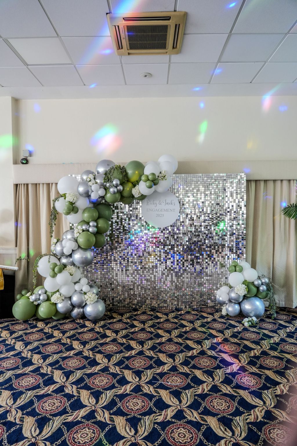 A room with a patterned carpet, a disco ball, and a decorative arch with balloons.