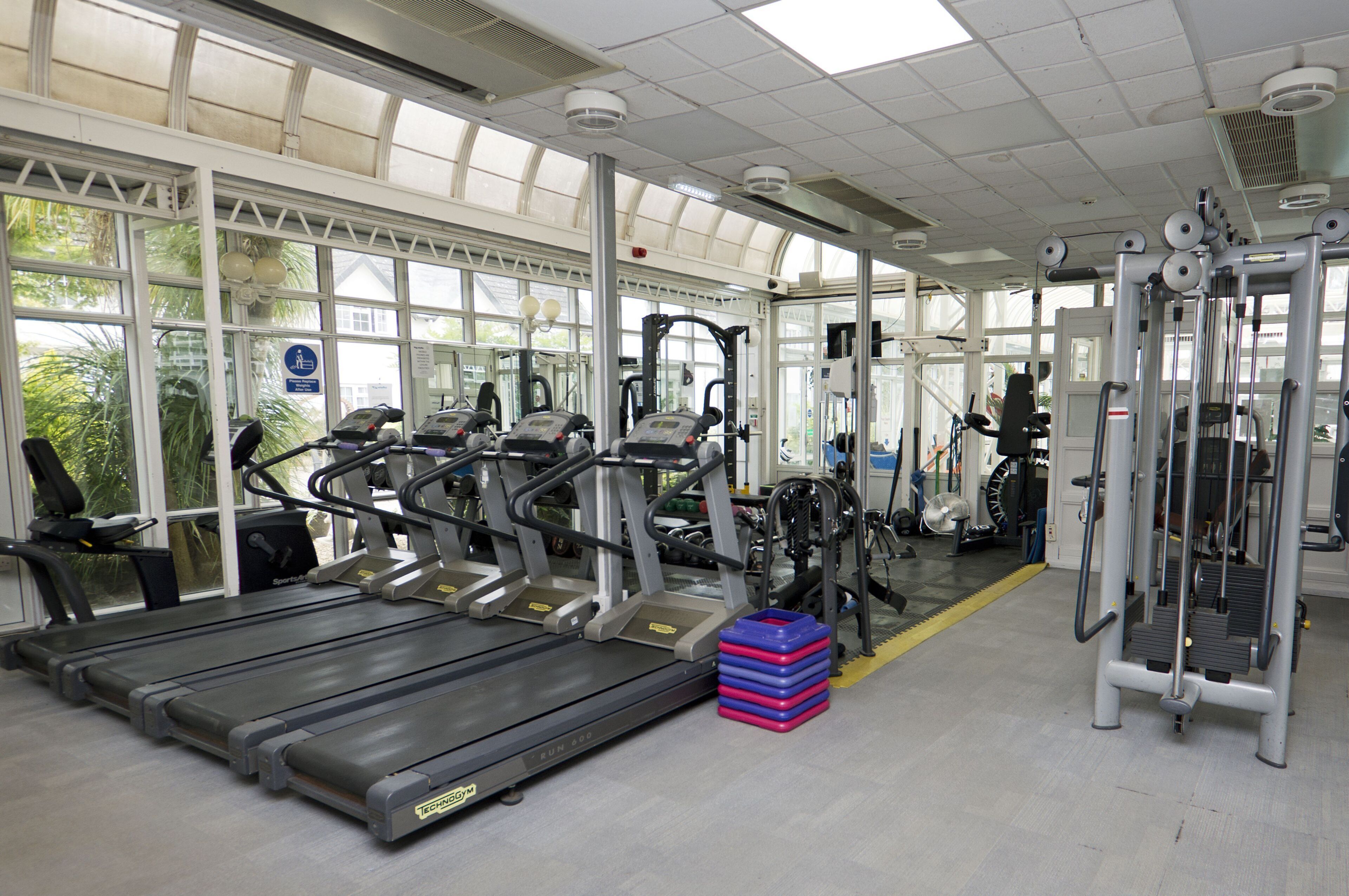 Un gimnasio con cintas de correr, máquinas de pesas y un amplio ventanal.