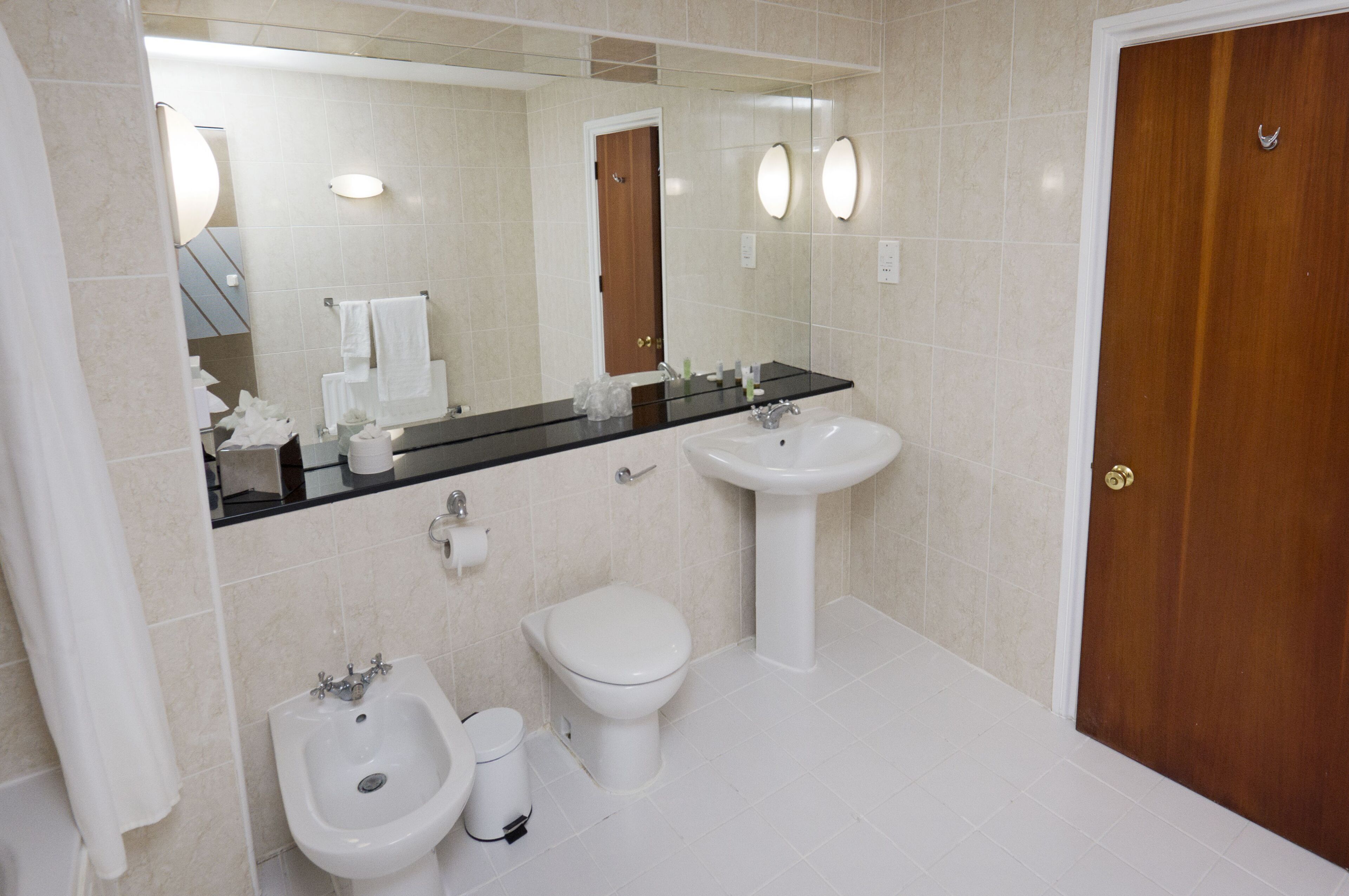Ein Badezimmer mit Bidet, Toilette, Waschbecken und einem Spiegel mit Beleuchtung.