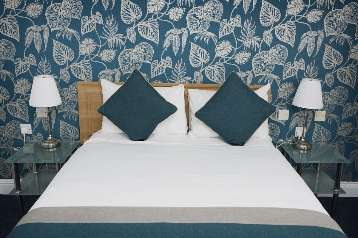 Une chambre d’hôtel avec un lit, deux tables de chevet, deux lampes et un papier peint à motifs floraux.