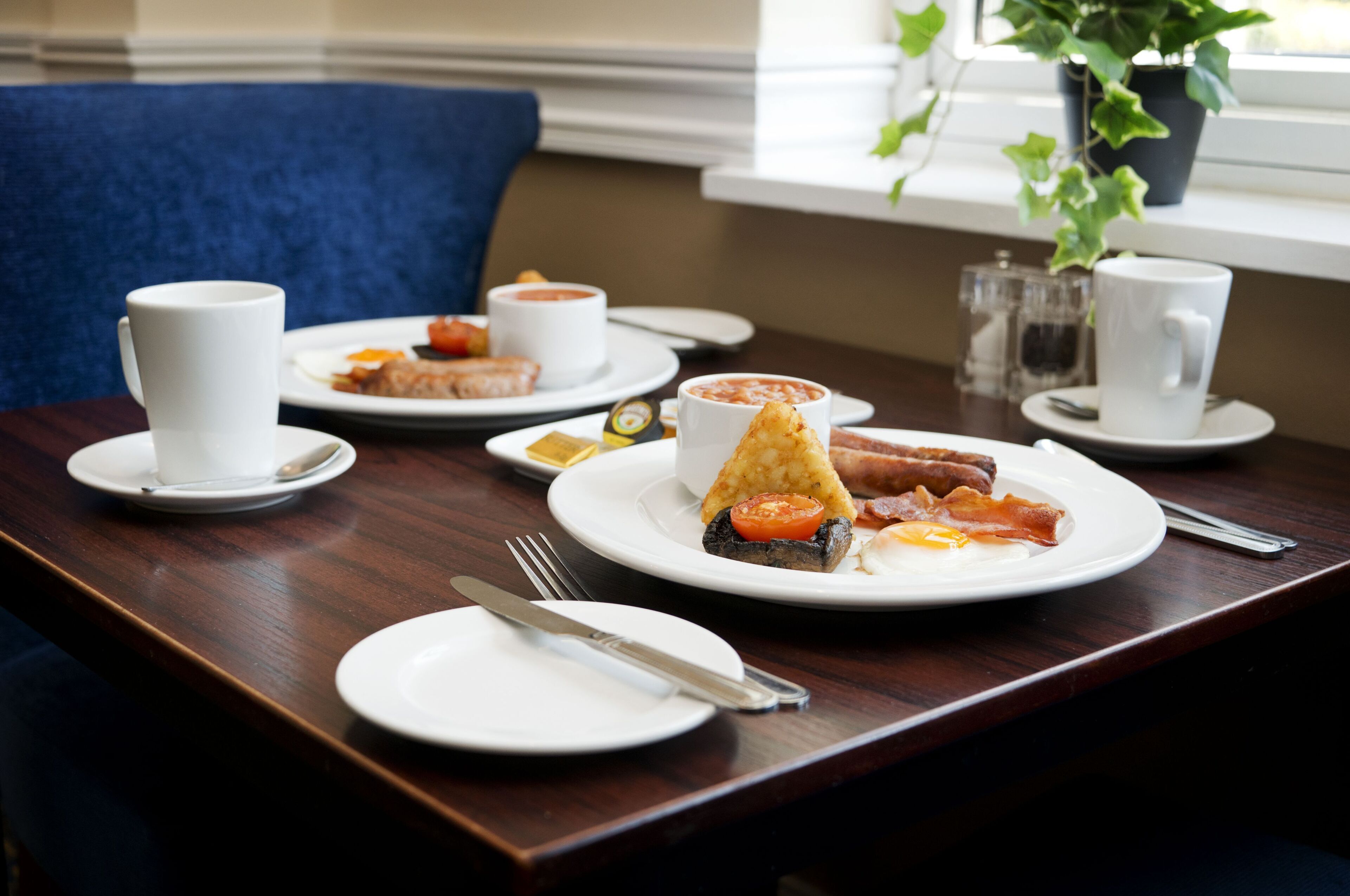 A breakfast setting with plates of food, cups, and cutlery on a wooden table.