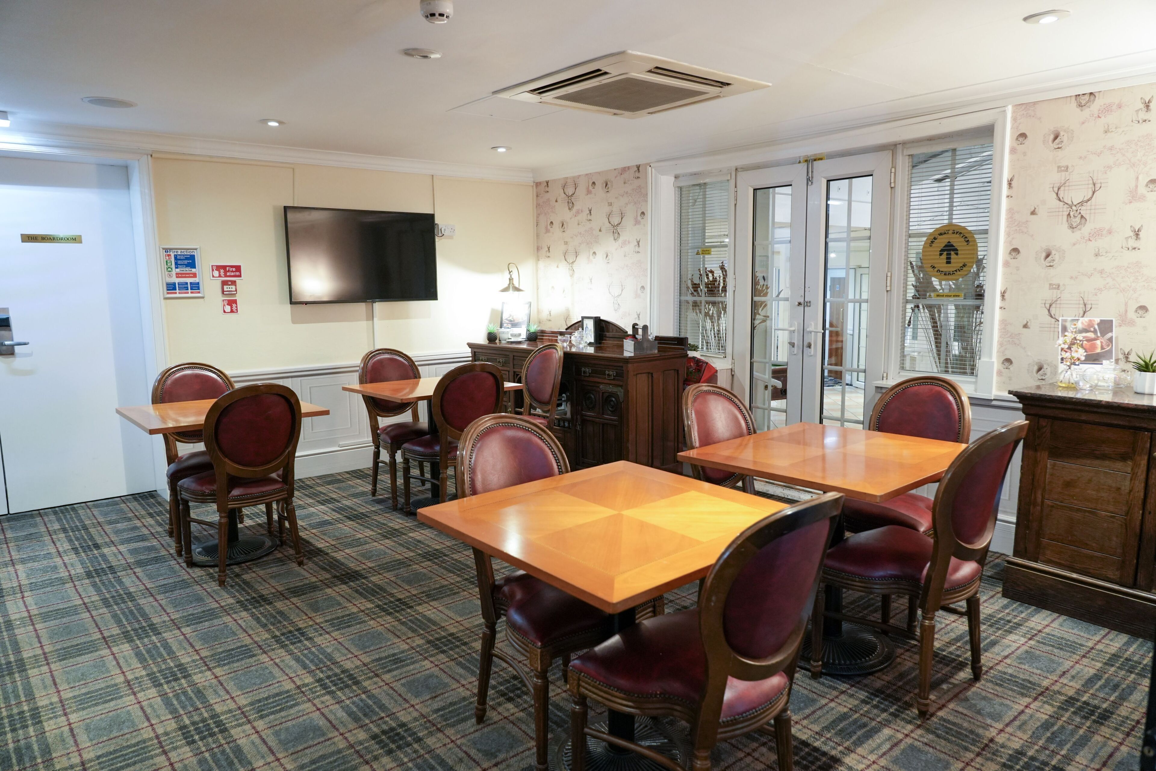 A conference room with plaid carpet, wooden tables and chairs, a flat-screen TV, and a decorative cabinet.