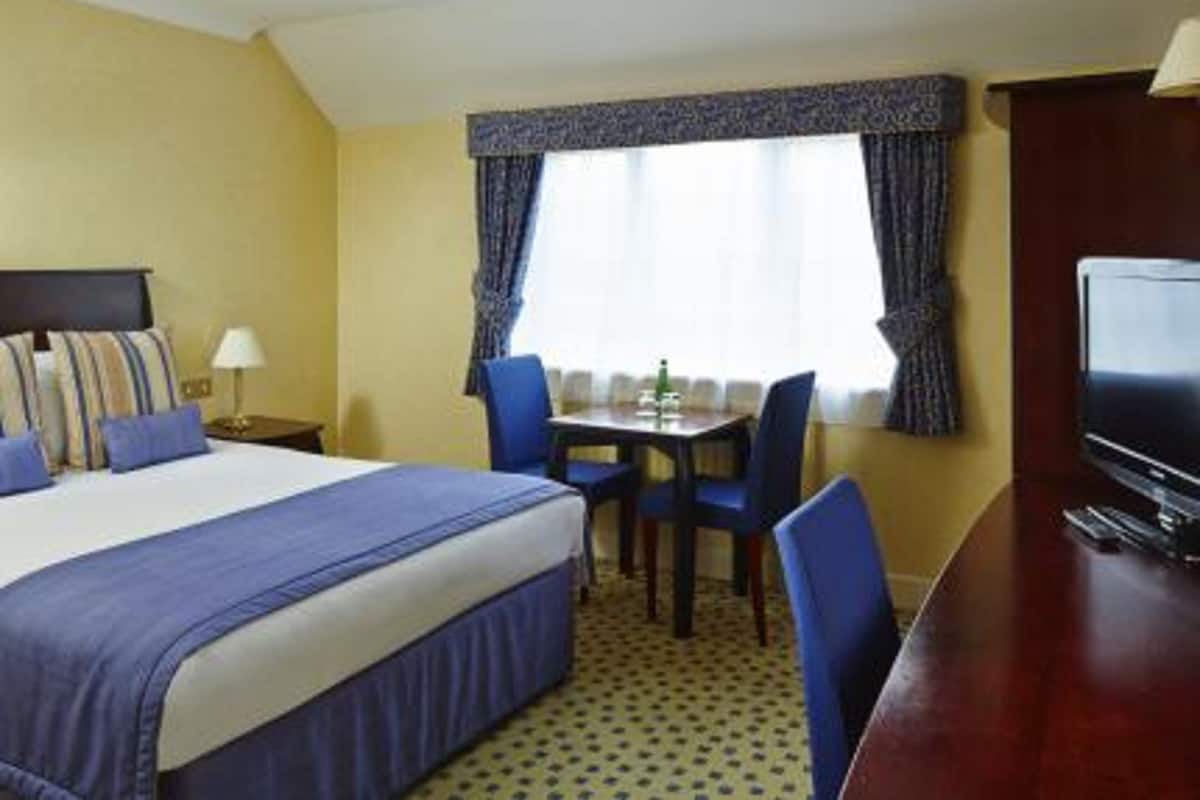Une chambre d’hôtel comprenant un lit, un bureau avec une chaise, une télévision et une fenêtre avec des rideaux.