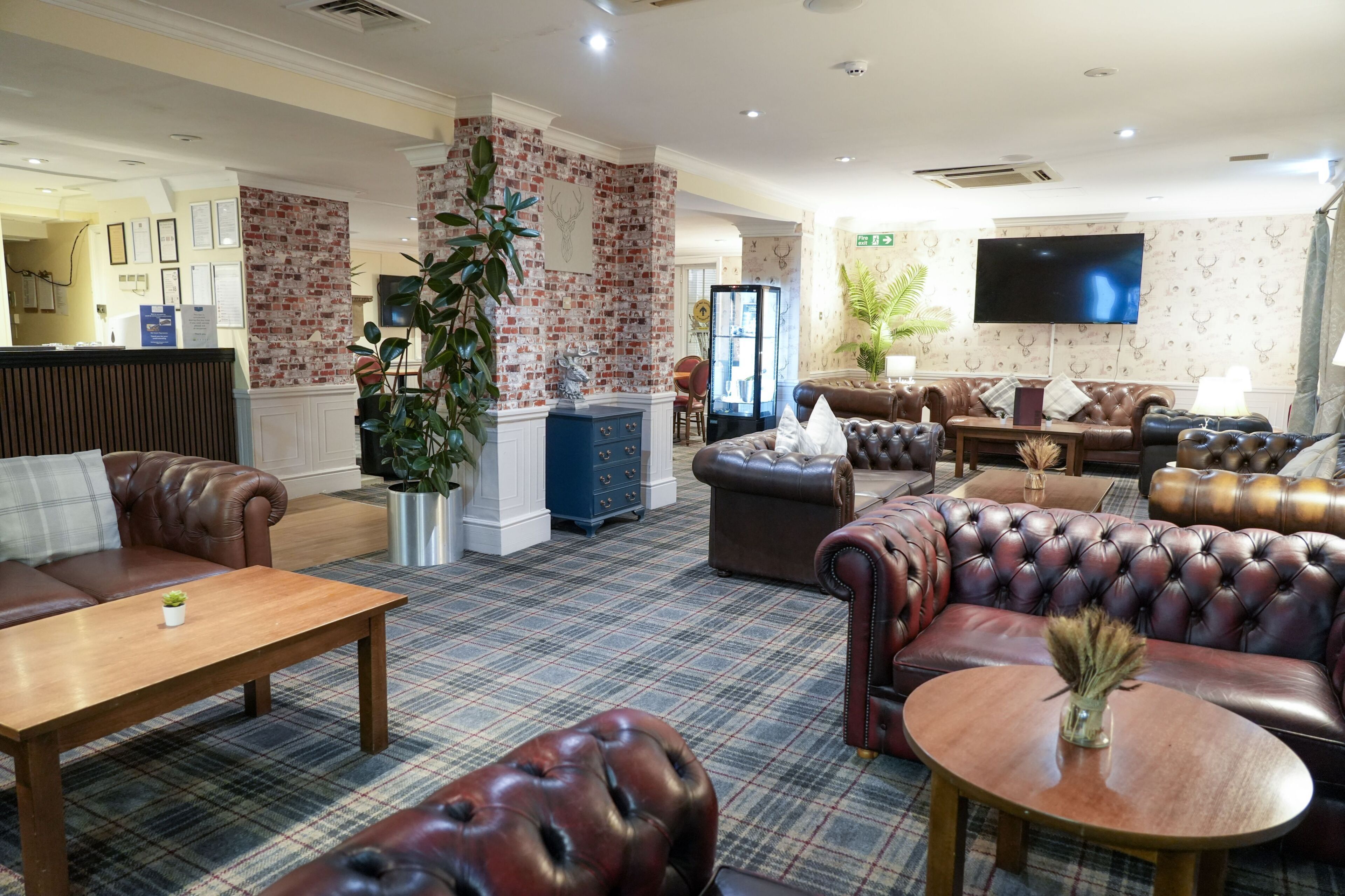 A lobby with leather sofas, a wooden coffee table, a brick accent wall, a flat-screen TV, and a reception desk.