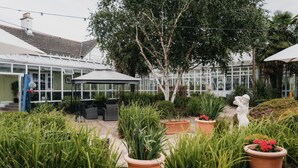 A conservatory with glass walls, outdoor seating, and potted plants. - Basingstoke Hotel (Hook)